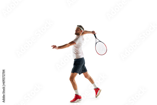 Full-length of young man in sportswear, tennis player practicing, hitting ball with racket isolated over white background. Concept of sport, hobby, active and healthy lifestyle, competition