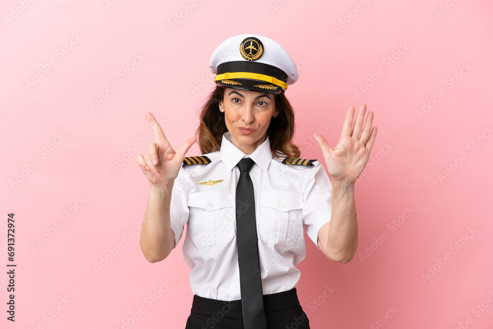 Airplane middle aged pilot woman isolated on pink background counting seven with fingers