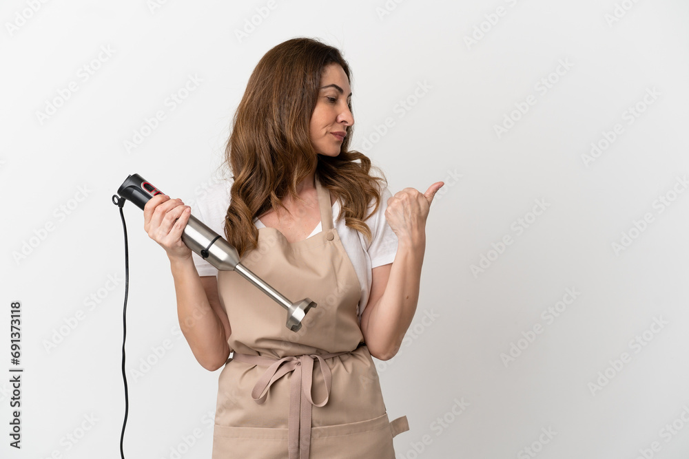 Middle aged caucasian woman using hand blender isolated on white background pointing to the side to present a product Middle aged caucasian woman using hand blender isolated on white background pointing to the side to present a product