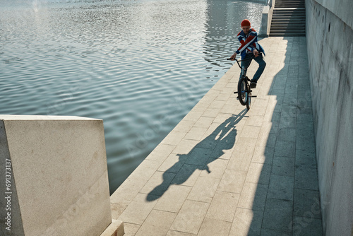 Man doing stunt with BMX bike near lake on embankment photo