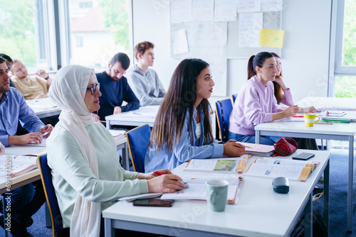 Multi-ethnic friends sitting at desks attending lecture in classroom photo