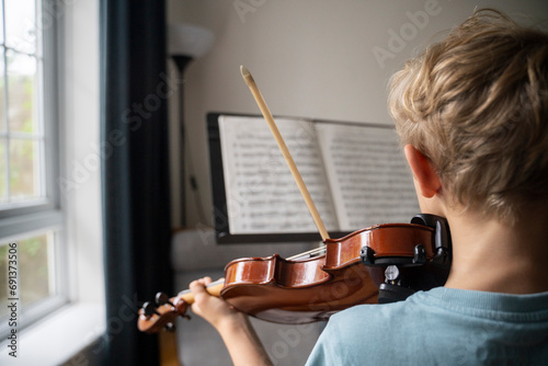 Boy practicing violin with sheet music at home photo