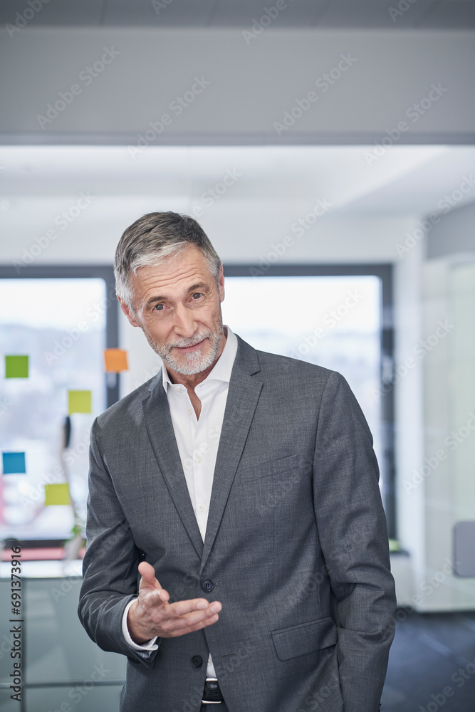 Smiling senior businessman gesturing and standing in office Smiling senior businessman gesturing and standing in office