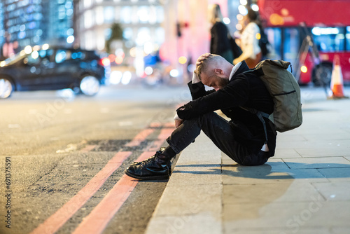 Depressed man with head in hand sitting on sidewalk in city photo