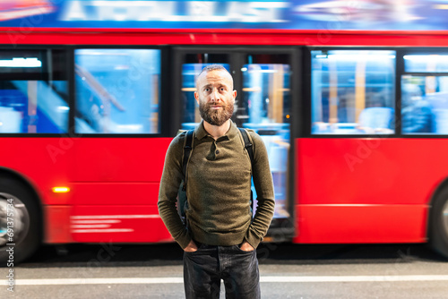 Man with hands in pockets standing in front of moving bus in city photo