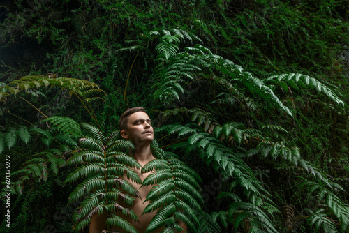 Shirtless man with eyes closed standing amidst fern plants photo