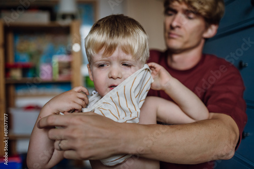 Photos Father putting shirt on little son, changing from pajamas in the morning