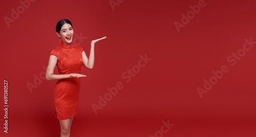 Happy Chinese new year. Asian woman wearing traditional cheongsam qipao dress with gesture of welcome isolated on red copy space background. photo