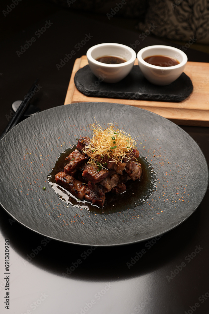 Fototapeta premium Grilled and sliced beef with sauce on a black plate, close-up