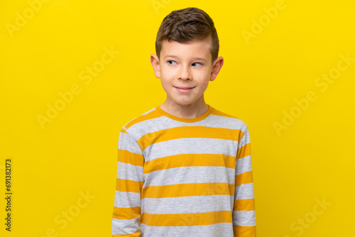 Little caucasian boy isolated on yellow background making doubts gesture looking side