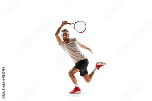 Dynamic image of concentrated young man, tennis player practicing, playing, hitting ball with racket isolated over white background. Concept of sport, hobby, active and healthy lifestyle, competition