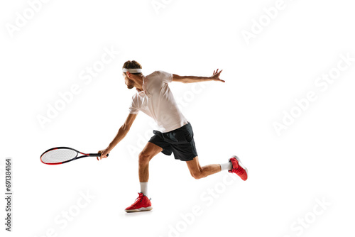 Dynamic image of concentrated young man, tennis player practicing, playing, hitting ball with racket isolated over white background. Concept of sport, hobby, active and healthy lifestyle, competition © master1305
