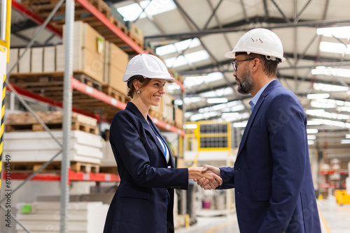 Female engineer and male project manager shaking hands in modern industrial factory. Manufacturing facility with robotics and automation. Women in manufacturing.