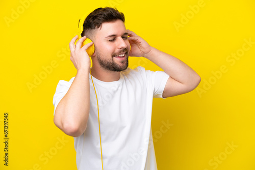 Young caucasian man isolated on yellow background listening music and singing