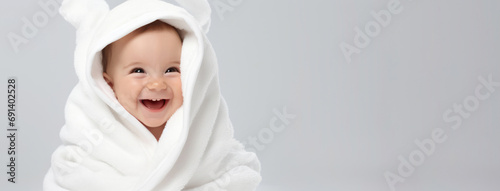 Smiling baby infant wrapped in white furry blanket. Portrait of happy adorable Caucasian little boy wrapped in fluffy towel after bath against light gray background. Textiles and bedding for children