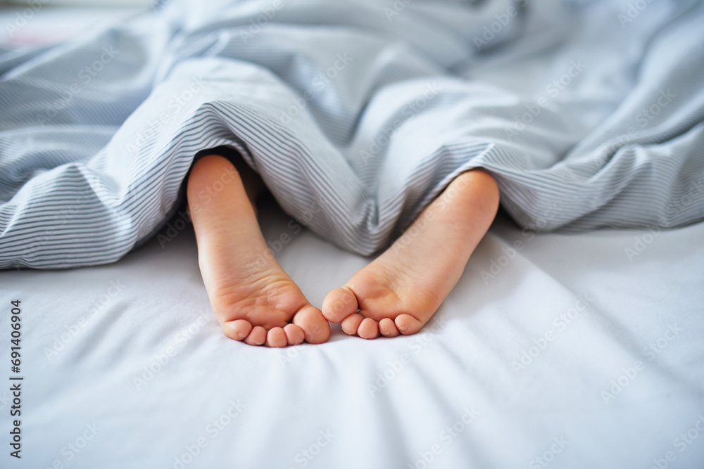 Little child's feet in bed covered with blanket - obrazy, fototapety, plakaty 