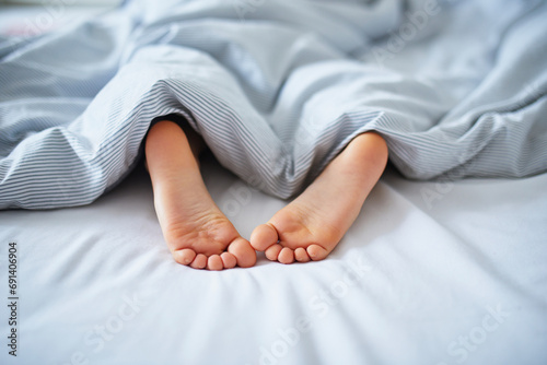 Little child's feet in bed covered with blanket