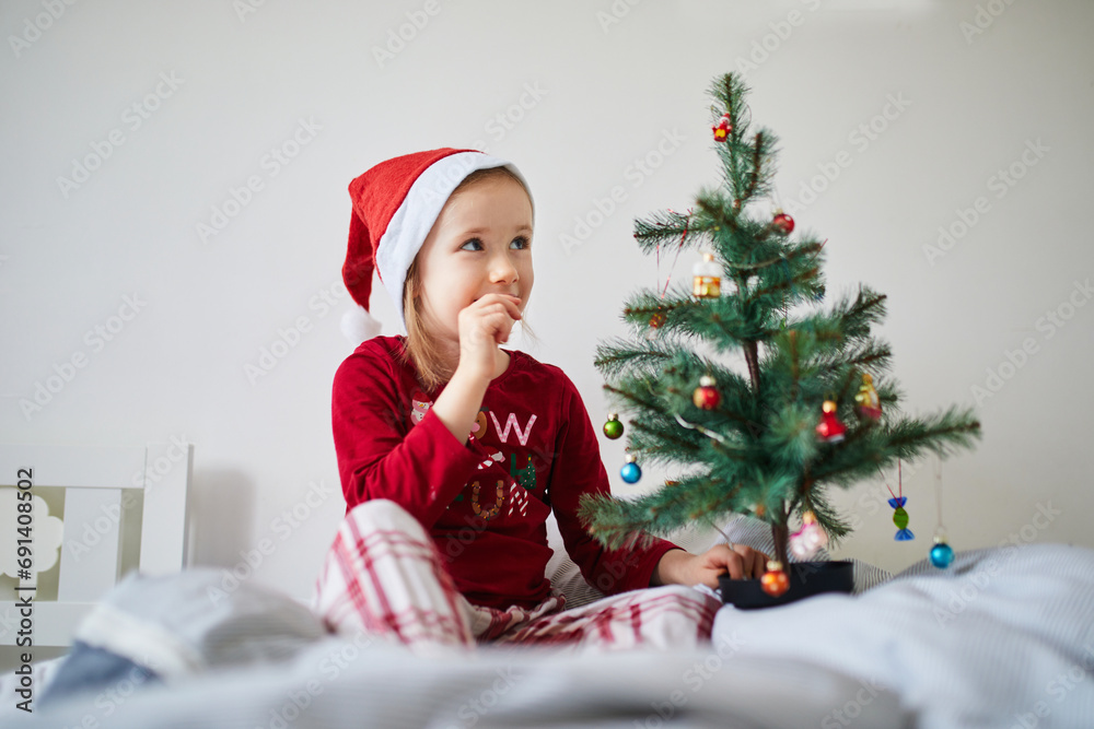 Happy preschooler girl wearing Christmas pajamas and playing with Christmas decorations on bed Happy preschooler girl wearing Christmas pajamas and playing with Christmas decorations on bed
