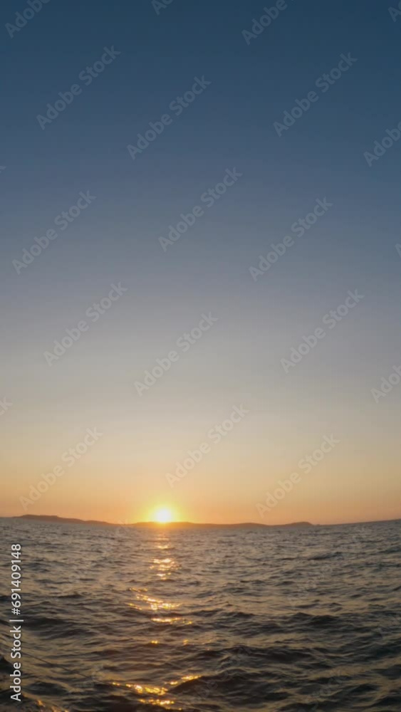 Slow-motion view of the sunset over Ons Island from a moving boat in the Pontevedra estuary. The clear summer sky is painted with hues of orange, reflecting in the shimmering waves below. Slow-motion view of the sunset over Ons Island from a moving boat in the Pontevedra estuary. The clear summer sky is painted with hues of orange, reflecting in the shimmering waves below.