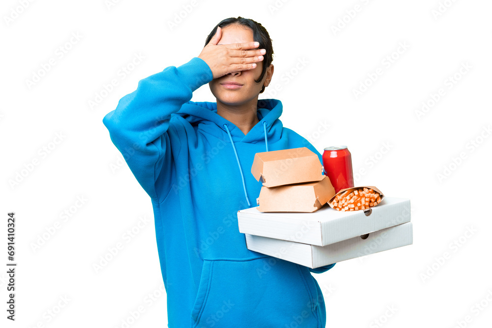 Young Uruguayan woman holding pizzas and burgers over isolated chroma key background covering eyes by hands. Do not want to see something Young Uruguayan woman holding pizzas and burgers over isolated chroma key background covering eyes by hands. Do not want to see something
