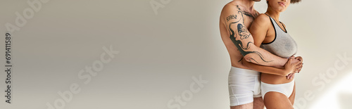cropped view of caring tattooed man hugging his african american girlfriend from behind, sexy couple