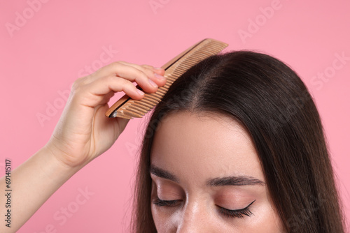 Woman with comb examining her hair and scalp on pink background, closeup