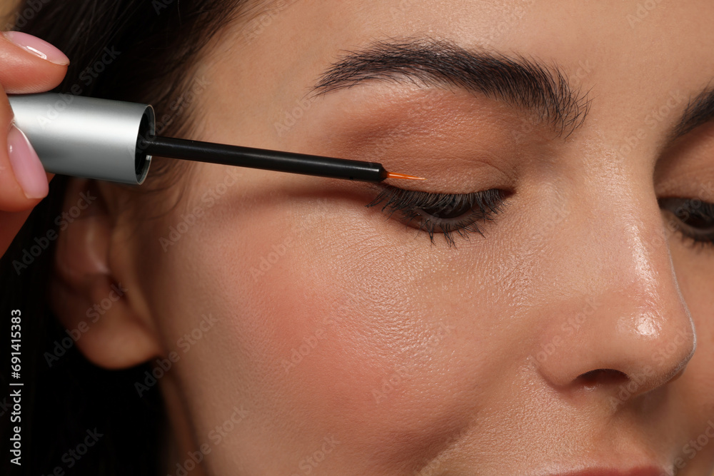 Woman applying serum onto her eyelashes, closeup. Cosmetic product