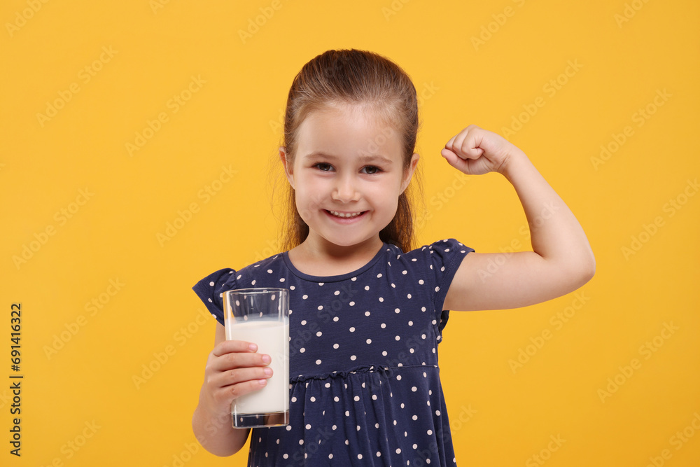 Cute girl with glass of fresh milk showing her strength on orange background - obrazy, fototapety, plakaty 