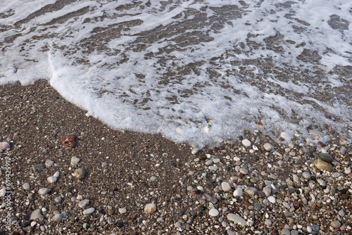 Lace foam of the sea wave on a pebble beach