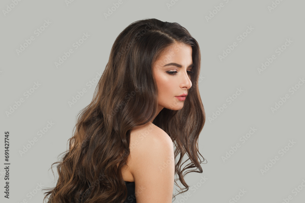Good-looking brunette fashion beauty portrait. Young model woman with long dark healthy hair and fresh clean skin on gray studio wall background