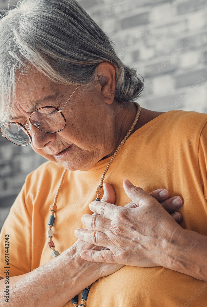 Obraz premium Upset stressed mature middle aged woman feeling pain ache touching chest having heart attack, sad worried senior older lady suffers from heartache at home, infarction or female heart disease concept.