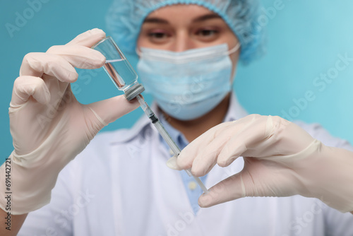 Doctor filling syringe with medication from glass vial on light blue background  selective focus