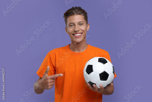Happy sports fan pointing at soccer ball on purple background © New Africa