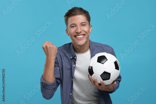Happy sports fan with soccer ball celebrating on light blue background © New Africa