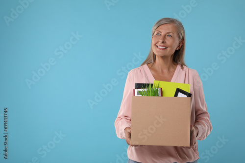 Happy unemployed senior woman with box of personal office belongings on light blue background. Space for text © New Africa