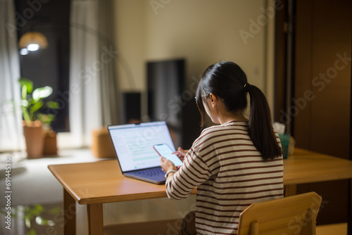 Woman work form home with laptop and use of mobile phone in the evening photo