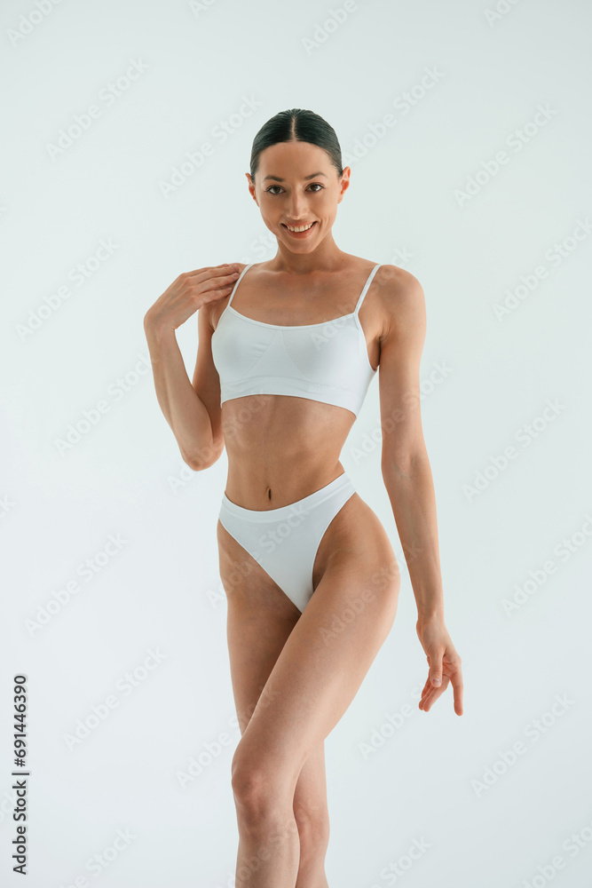 Feeling good. Standing and smiling. Young woman with slim body type is in fitness clothes in the studio Feeling good. Standing and smiling. Young woman with slim body type is in fitness clothes in the studio