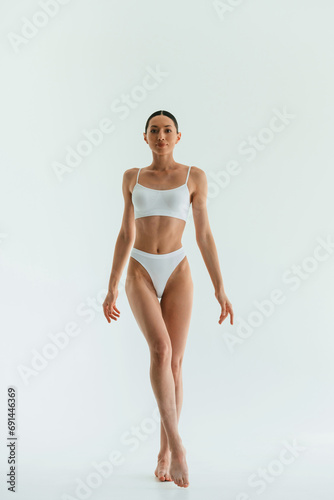 Against white background. Young woman with slim body type is in fitness clothes in the studio