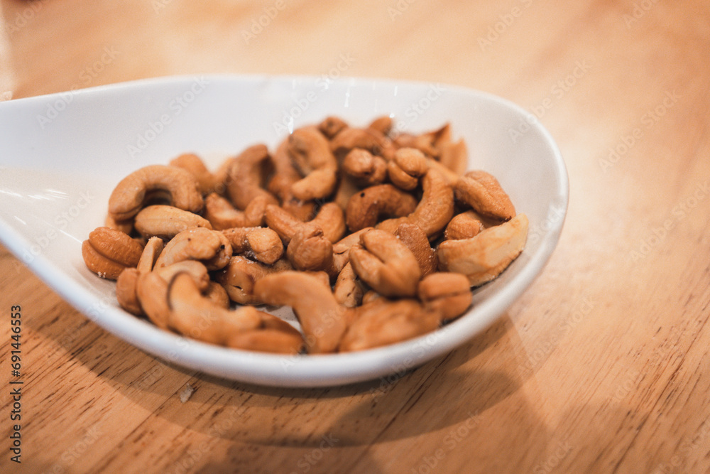 Tasty cashew nuts in white bowl on a wood table. Food concept. Tasty cashew nuts in white bowl on a wood table. Food concept.