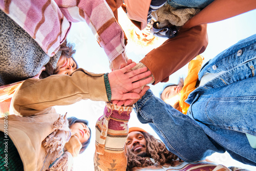Low angle view of multiracial group of friends joining hands together in cooperation. photo