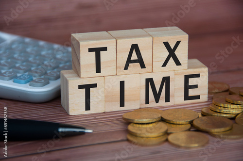 Tax time text on wooden blocks with gold coins, pen and calculator. Tax concept