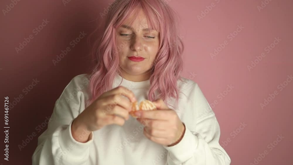 Happy pink hair woman eats a tangerine, orange fruit isolated on pink background in studio. High quality FullHD footage Happy pink hair woman eats a tangerine, orange fruit isolated on pink background in studio. High quality FullHD footage