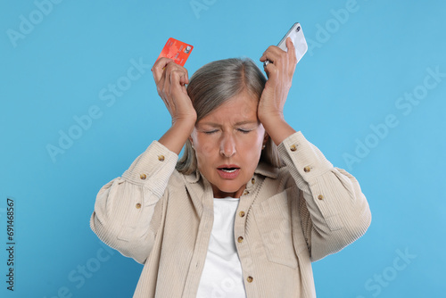 Fotografie Upset woman with credit card and smartphone became a fraud victim on light blue