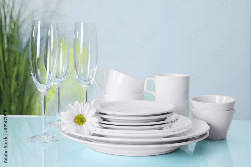 Set of clean dishware and flower on light blue table