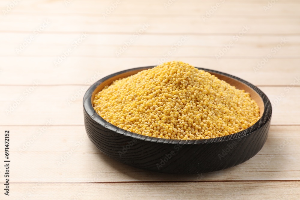 Millet groats in bowl on light wooden table, space for text Millet groats in bowl on light wooden table, space for text