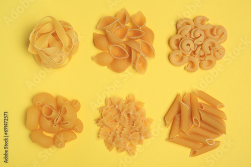 Different types of pasta on yellow background, flat lay photo