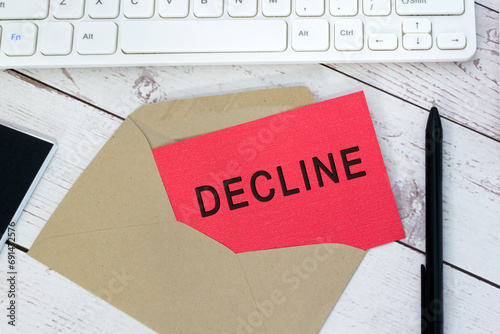 Decline text on red card with envelope, white keyboard and pen on wooden table.