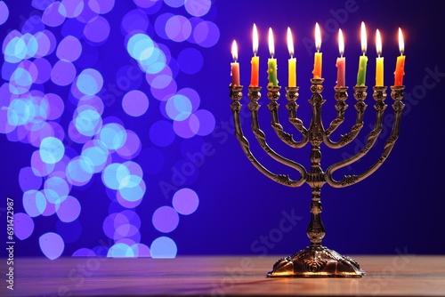 Hanukkah celebration. Menorah with burning candles on table against blue background with blurred lights, space for text