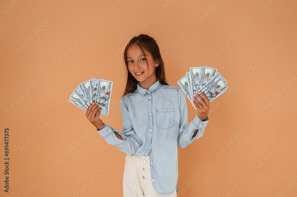 With bunch of currency, rich. Cute young girl is in the studio against background With bunch of currency, rich. Cute young girl is in the studio against background