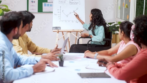 Businesswoman on wheelchair explaining from white board during team meeting at office - concept of empowerment, corporate planning and inspiration or motivation.